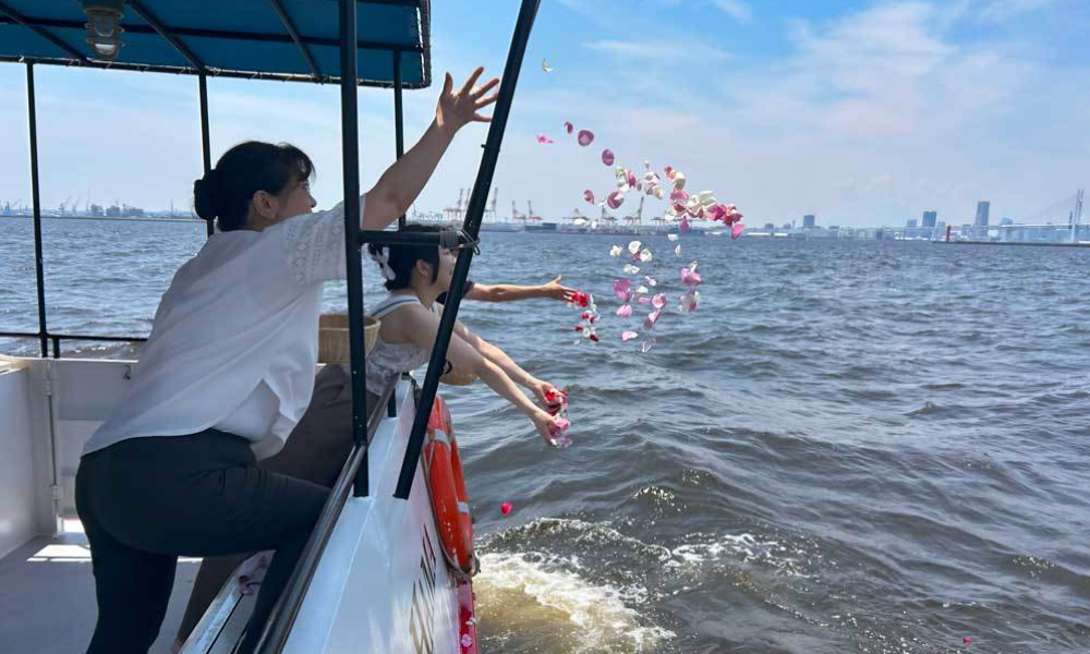 横浜ベイブリッジ沖で色とりどりの花を海に撒き、波間に広がる花々を見送りながら手を合わせる家族